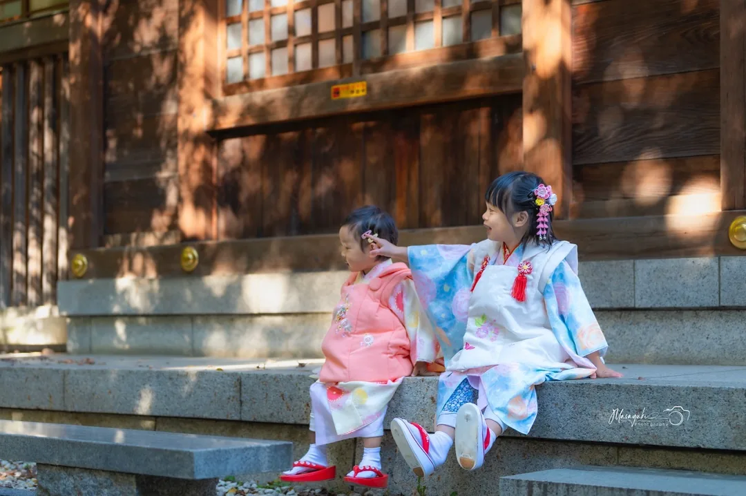 神社の石段に並んで座る着物姿の姉妹