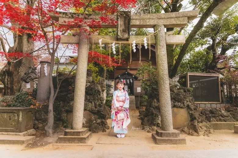 紅葉の鳥居の下に立つ着物姿の女の子